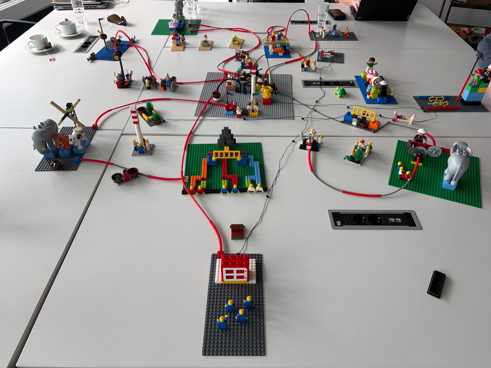 A team's system built in LEGO on the table: individual models linked by red and grey connections, all leading to one model at the bottom